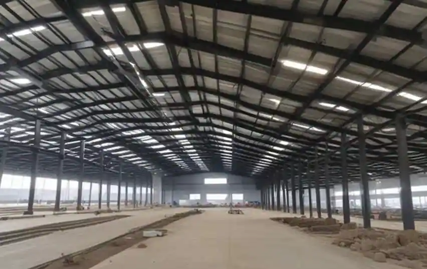 Wide interior view of a massive pre-engineered building industrial warehouse showing the steel rafter beams, columns, and roof purlins during the on-site erection phase